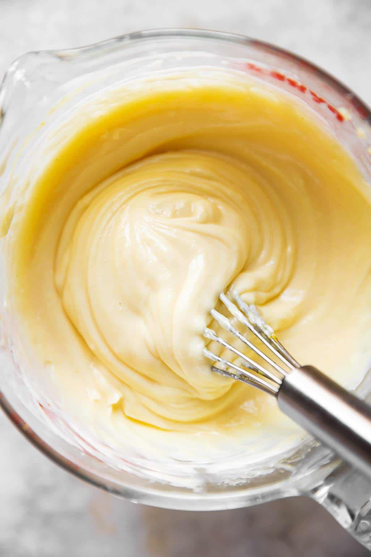 overhead view of homemade mayonnaise in glass measuring jug with metal whisk stuck in