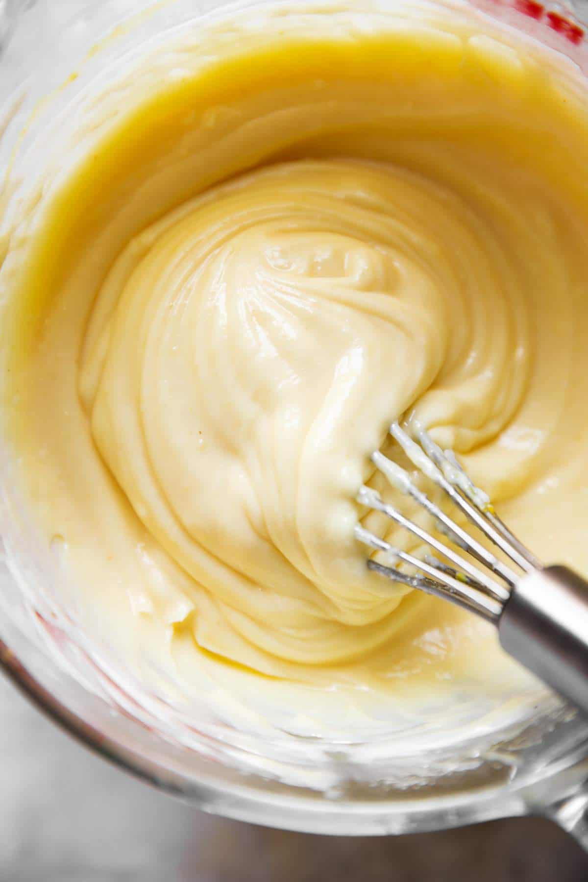 close up photo of homemade mayonnaise in glass measuring jug with metal whisk