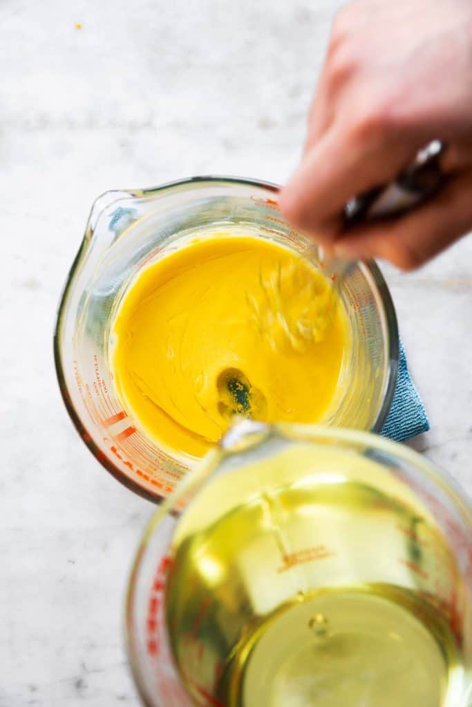 female hand pouring oil into glass measuring jug with whisked egg yolks