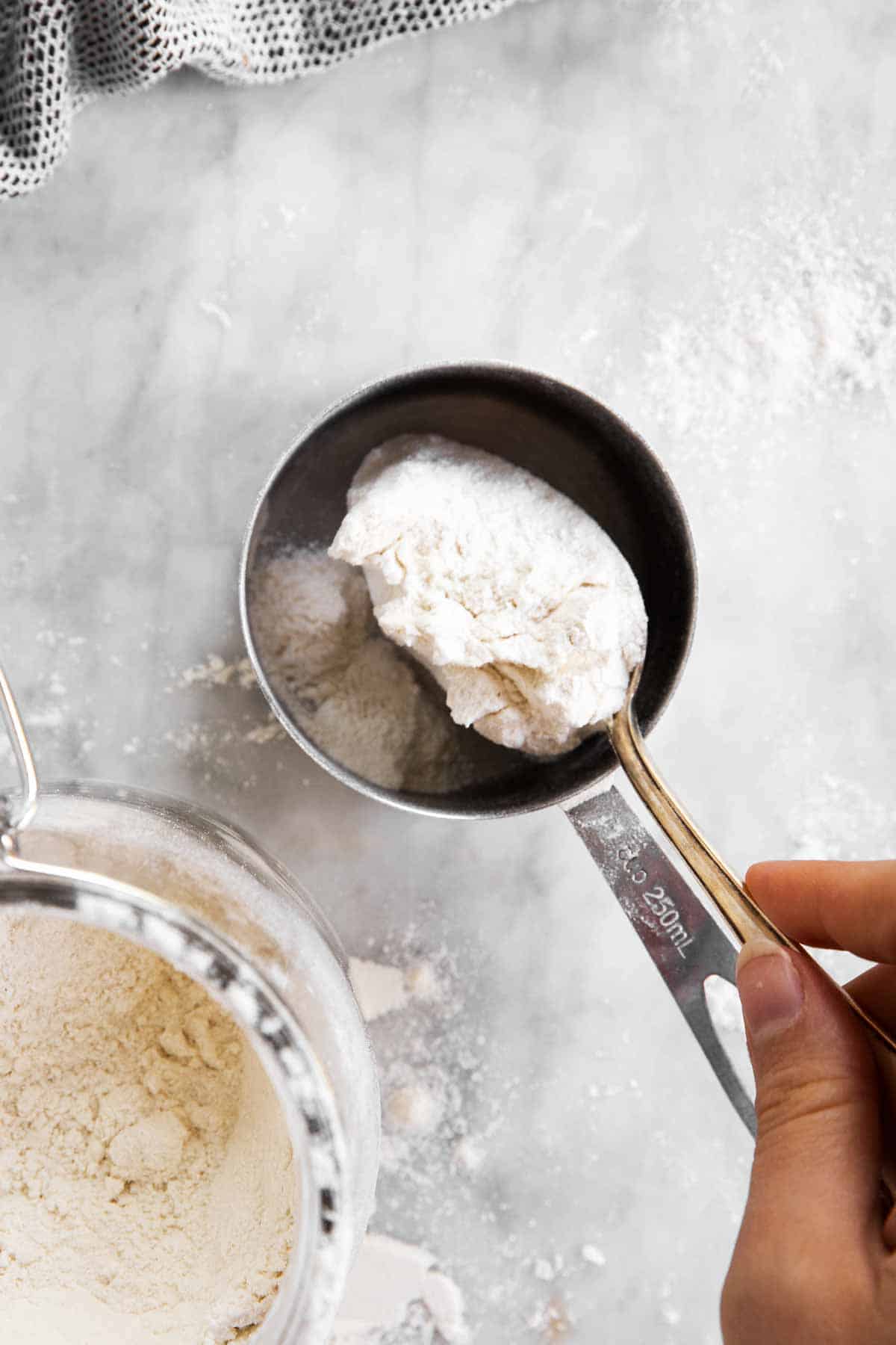 female hand using large spoon to add flour to measuring cup