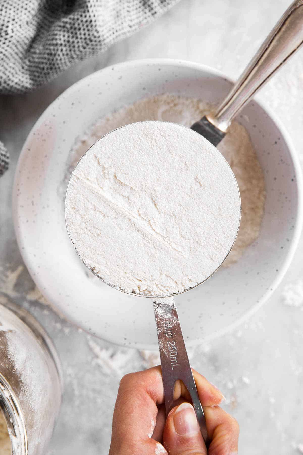 female hand holding cup measurement filled with flour