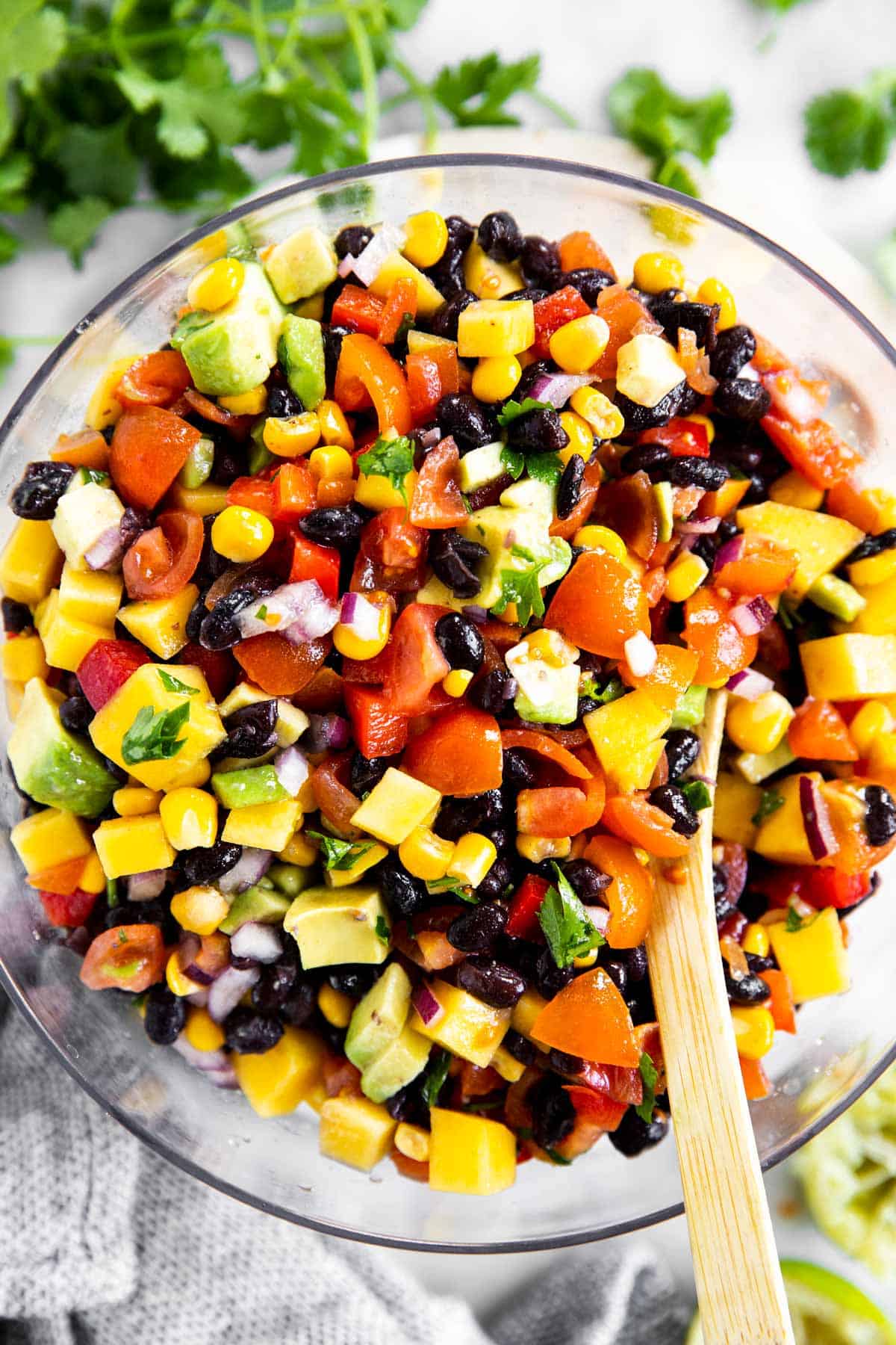 overhead view of glass bowl with mango black bean salsa surrounded by lime wedges and fresh cilantro