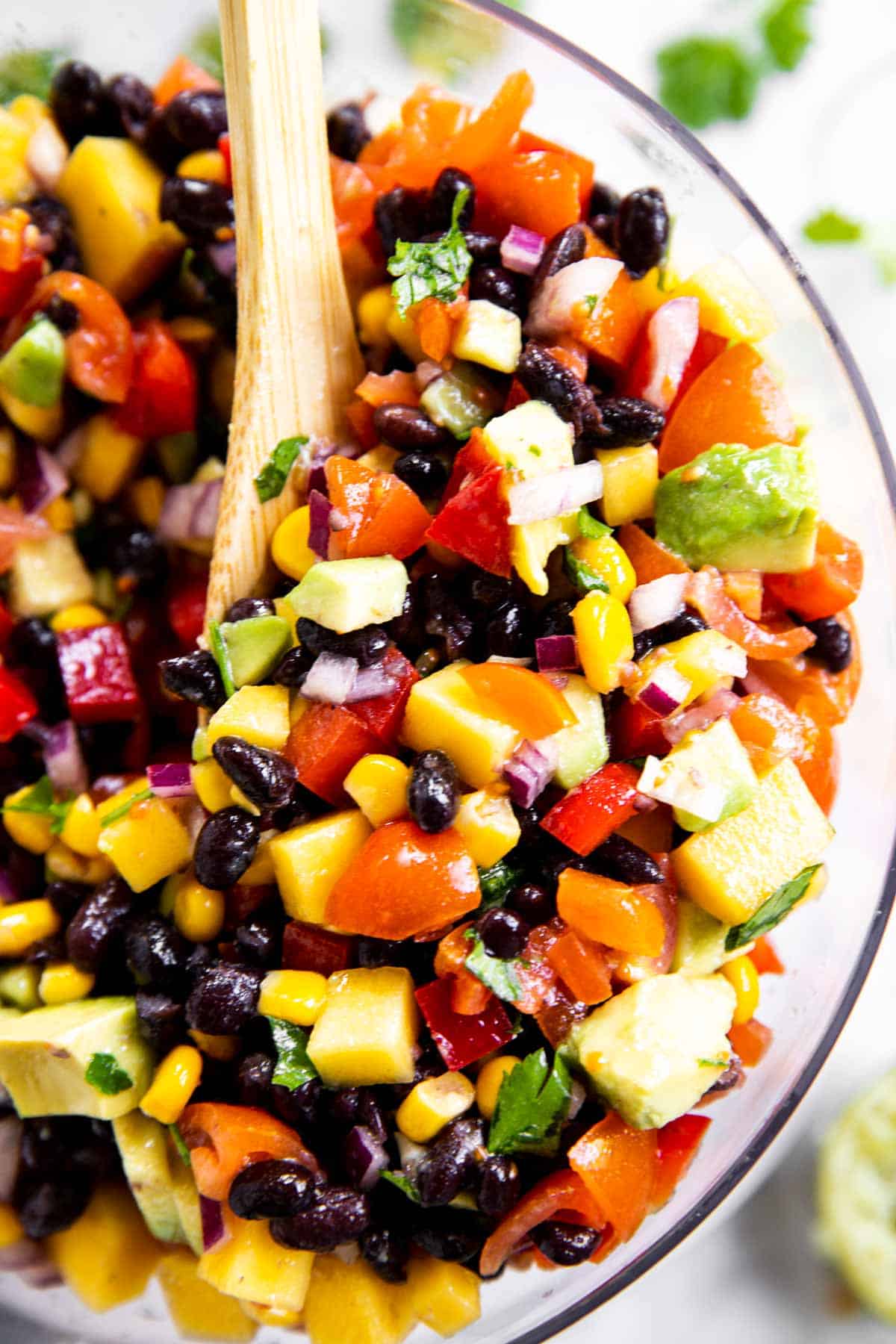 overhead close up view of mango black bean salsa in glass bowl with wooden spoon