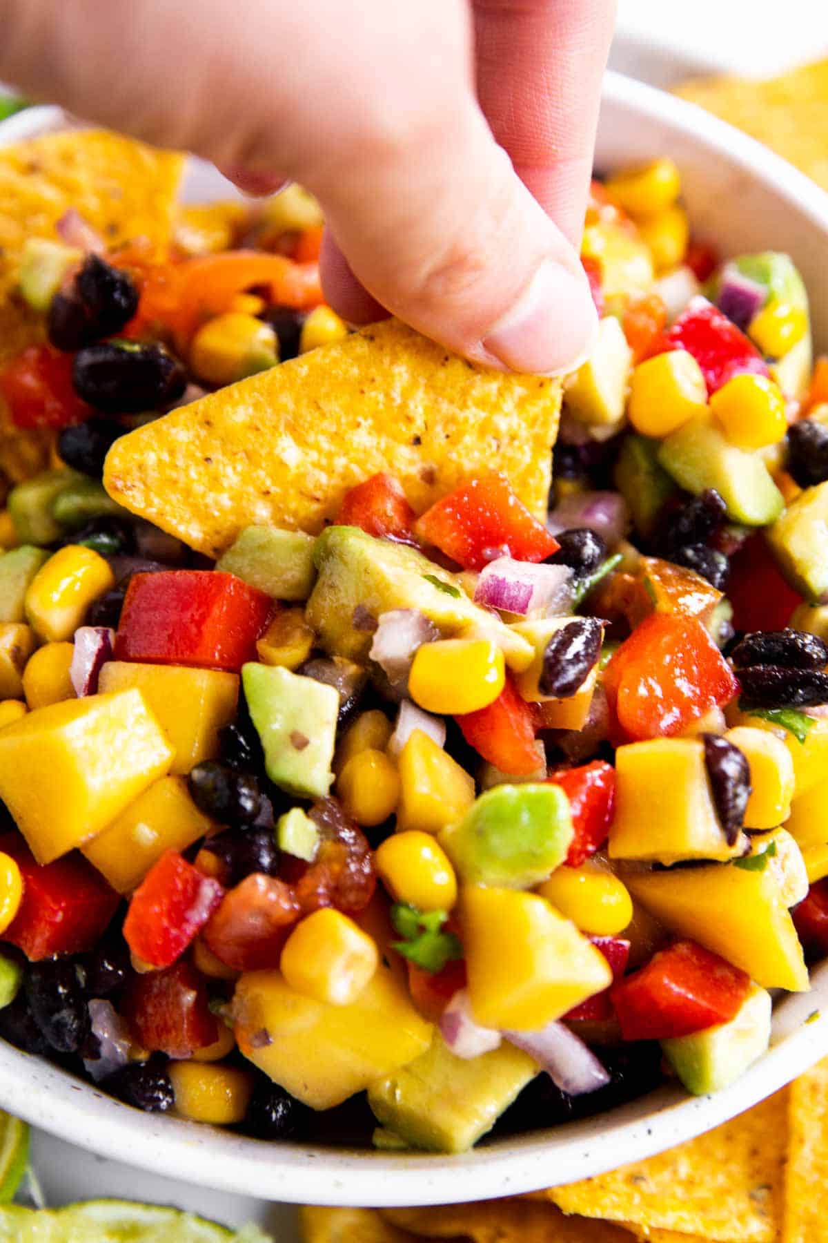 female hand dipping corn chip into mango black bean salsa