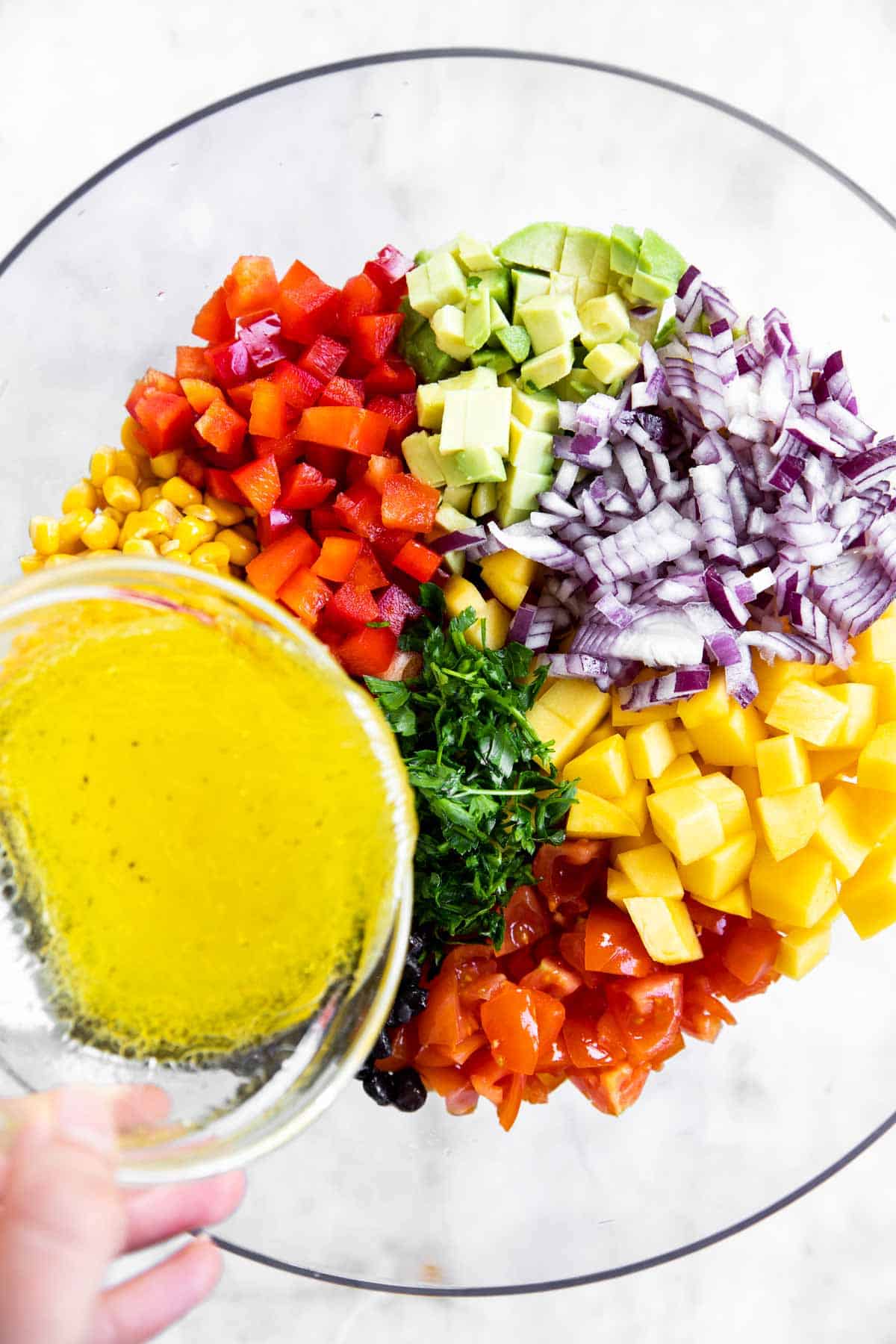 female hand pouring lime juice over chopped salsa ingredients in glass bowl