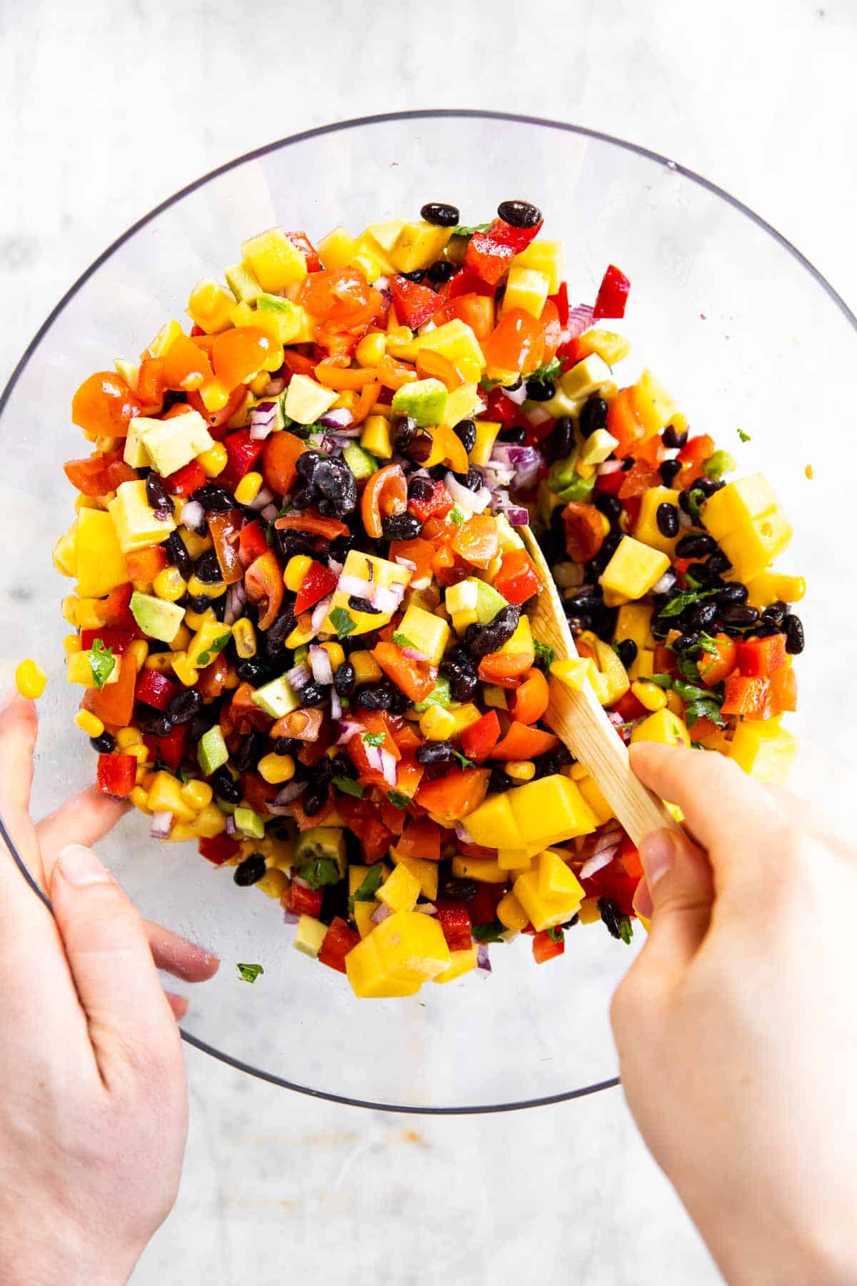 female hands stirring black bean salsa in glass bowl