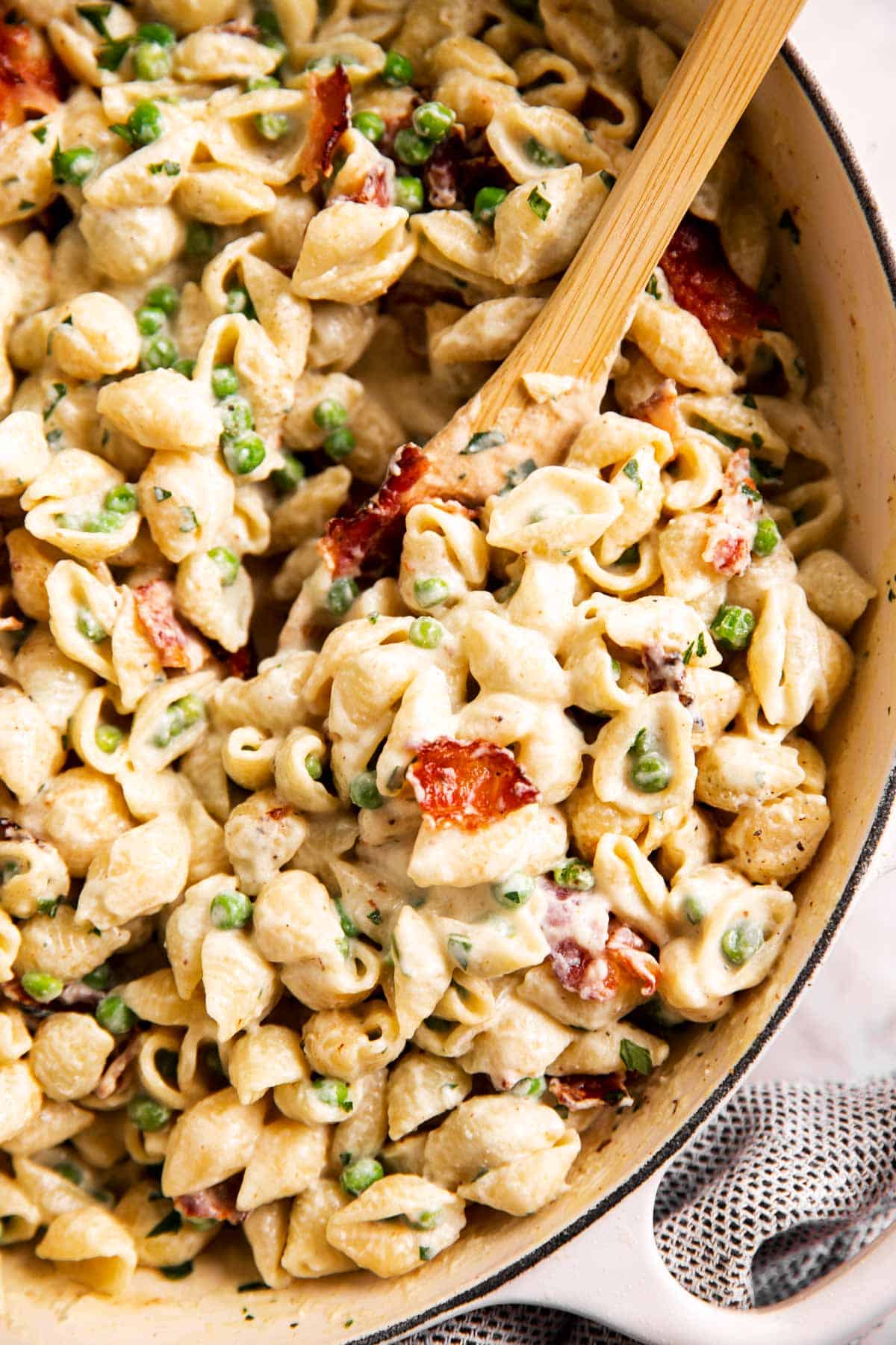close up view of pea and bacon pasta in white skillet with wooden spoon