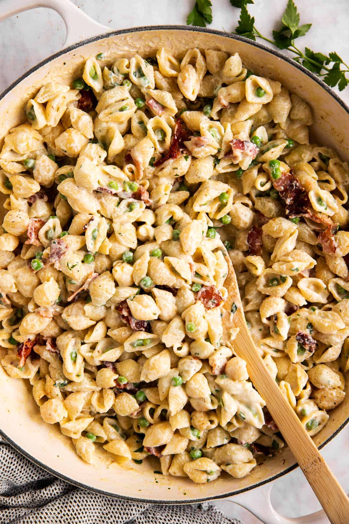 overhead view of pea and bacon pasta in white pot with wooden spoon