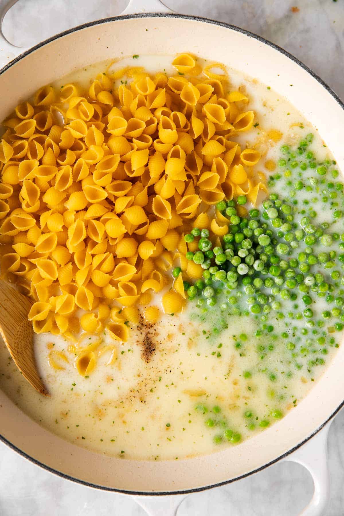 uncooked pasta and frozen peas with milk and broth in white skillet