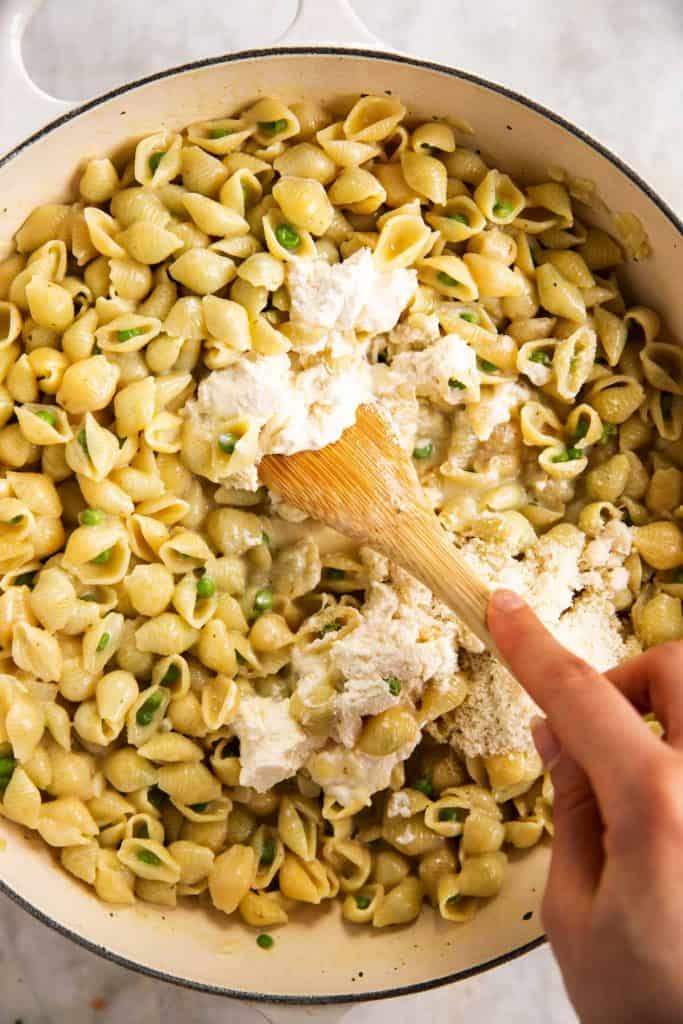 female hand stirring ricotta cheese into cooked pasta and peas