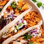 overhead view of pineapple bbq pulled chicken tacos on white plate with fresh cilantro