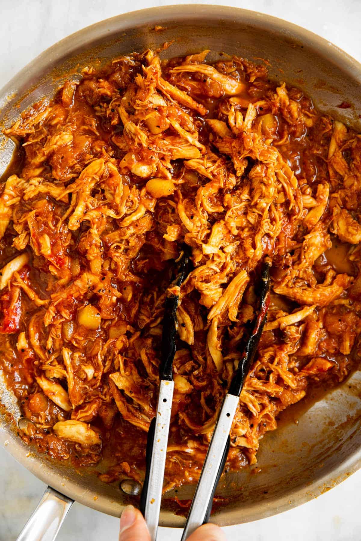 pineapple BBQ pulled chicken in stainless steel skillet with kitchen tongs