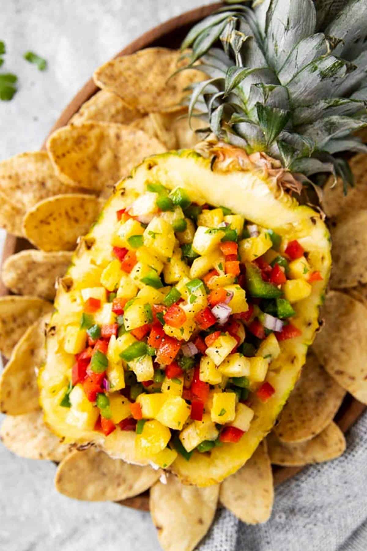 halved and hollowed out pineapple filled with pineapple salsa on a bed of corn chips