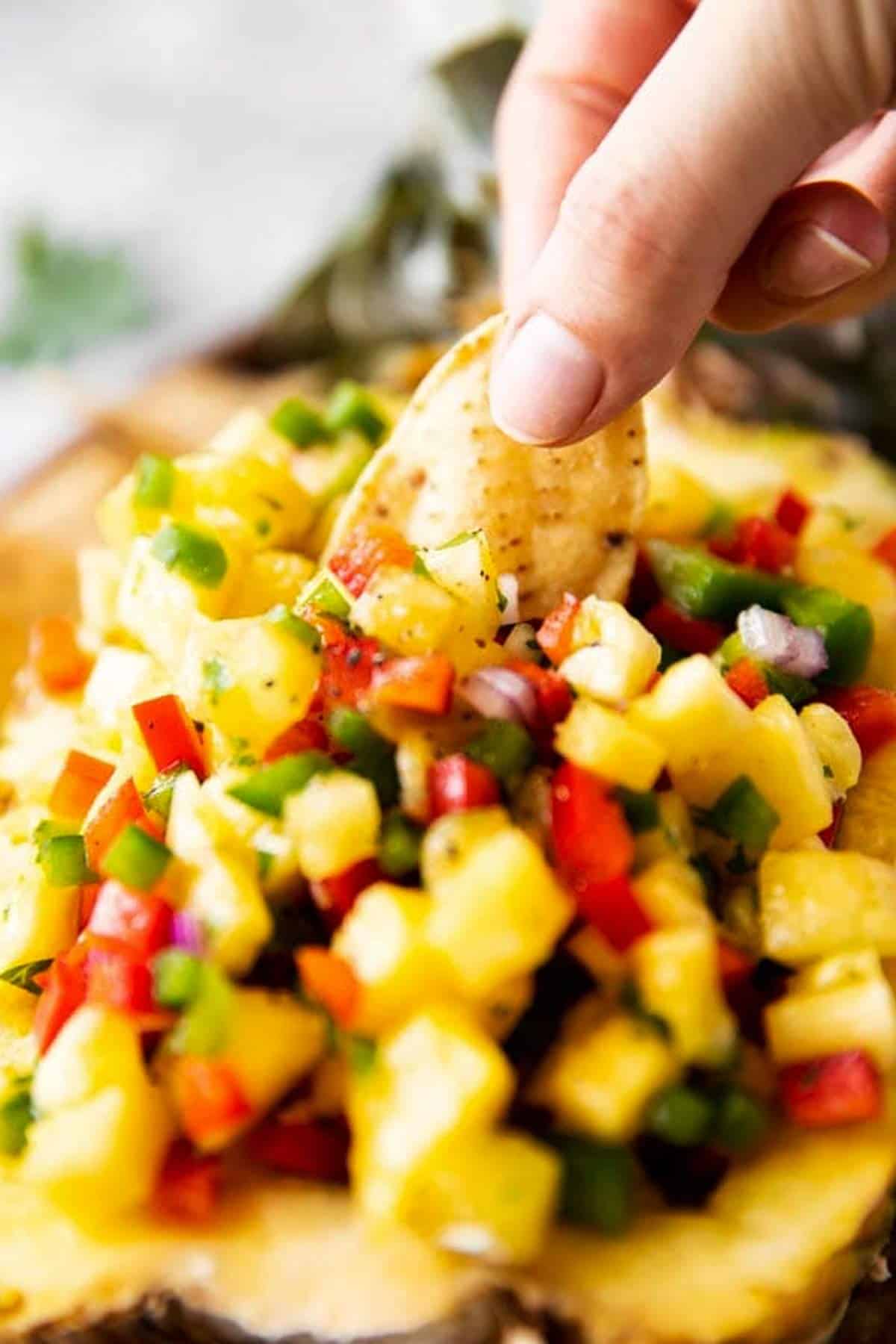 female hand scooping pineapple salsa with a corn chip