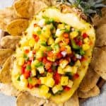 halved and hollowed out pineapple filled with pineapple salsa on a bed of corn chips
