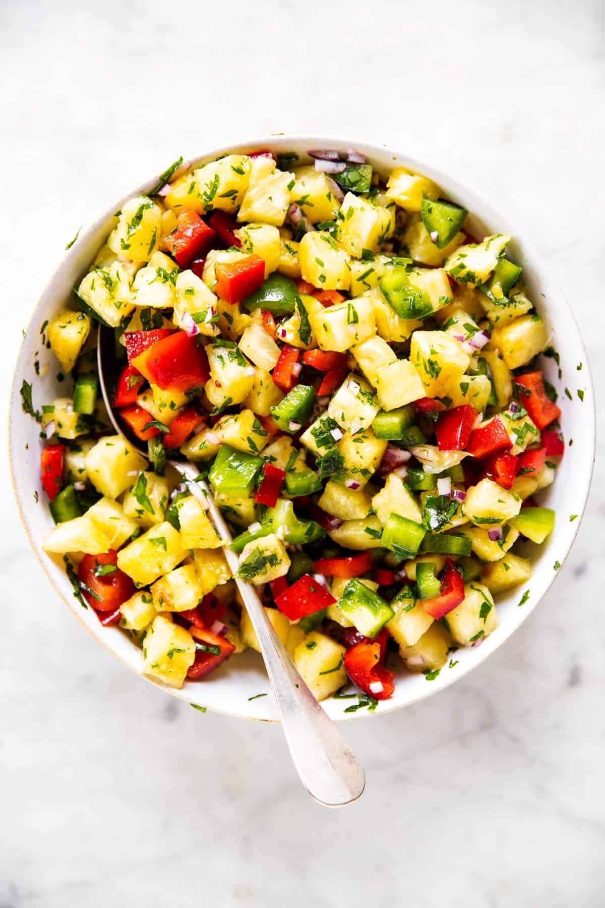 mixed pineapple salsa in white bowl with spoon stuck in