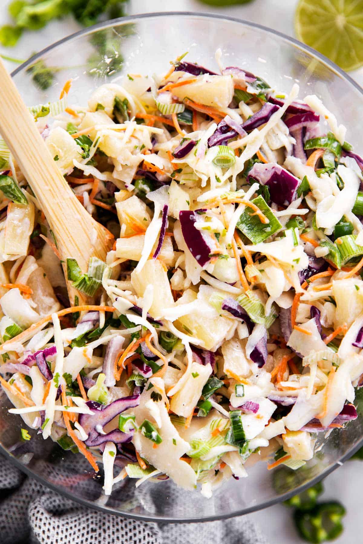 pineapple coleslaw in glass bowl with wooden salad tongs