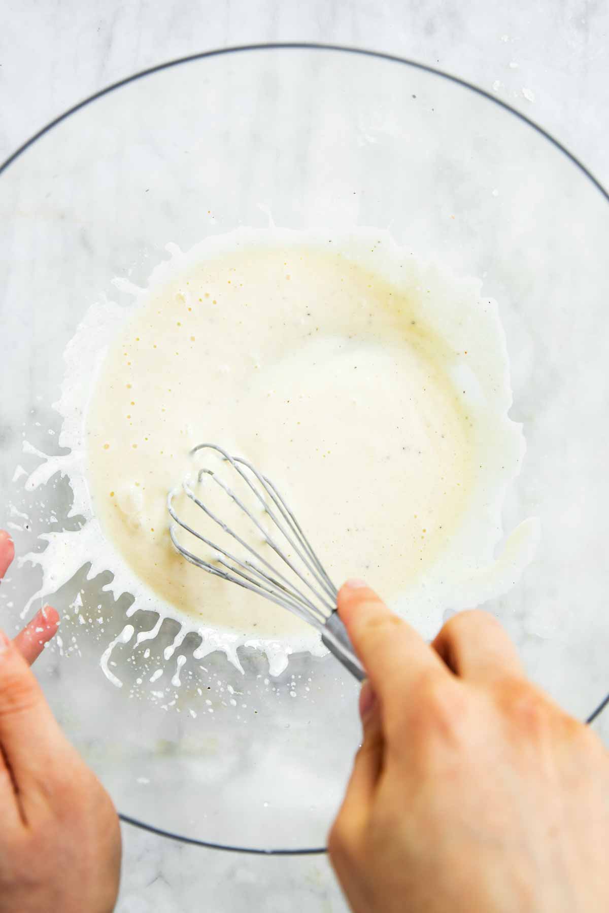 female hands whisking mayonnaise dressing in glass bowl