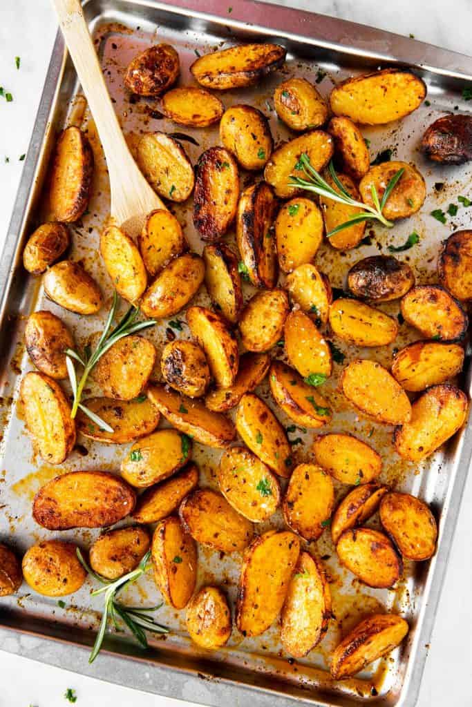 roasted baby potatoes on metal sheet pan with fresh rosemary, parsley and a wooden spoon
