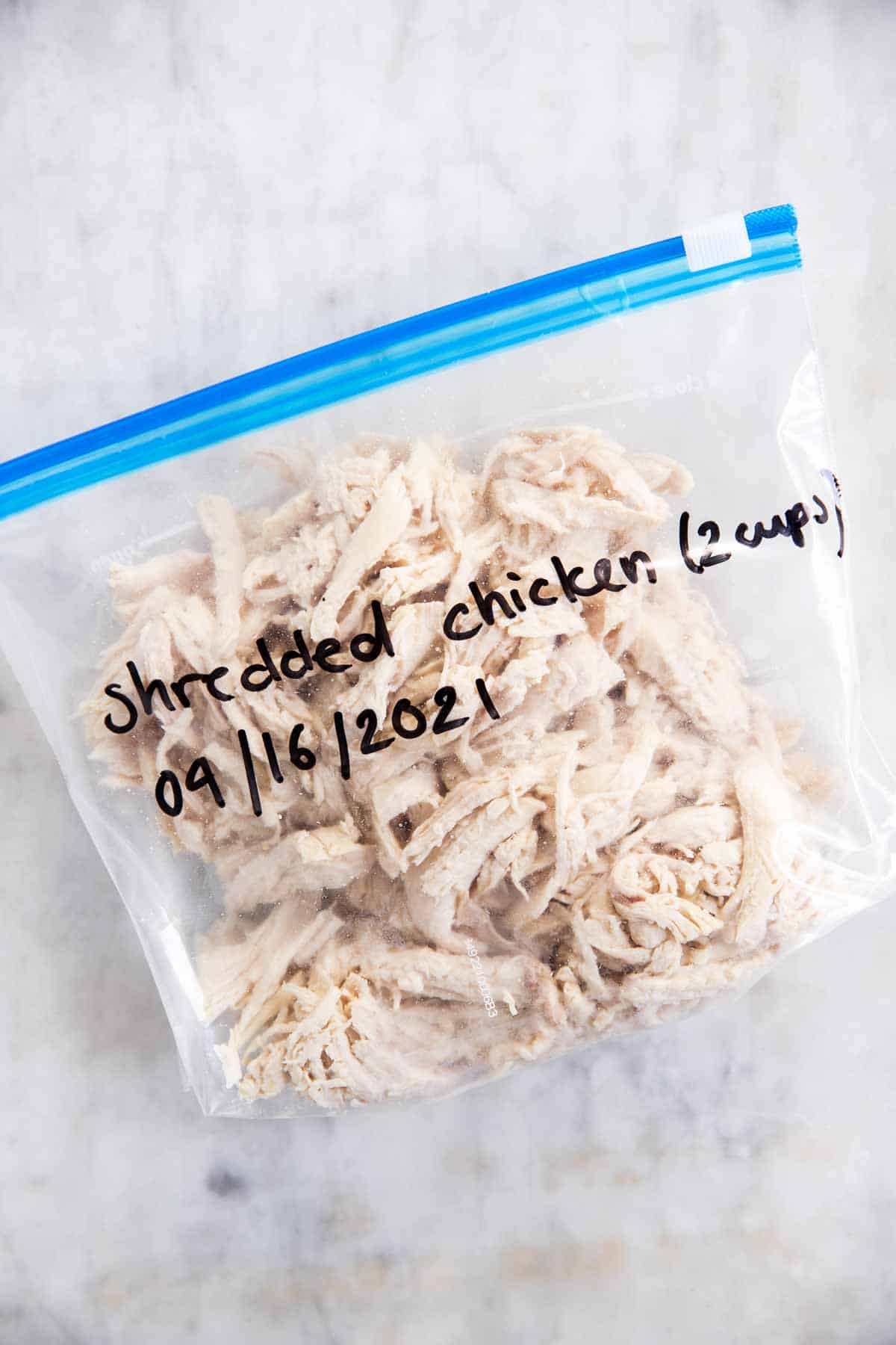 freezer bag filled with shredded chicken on marble surface