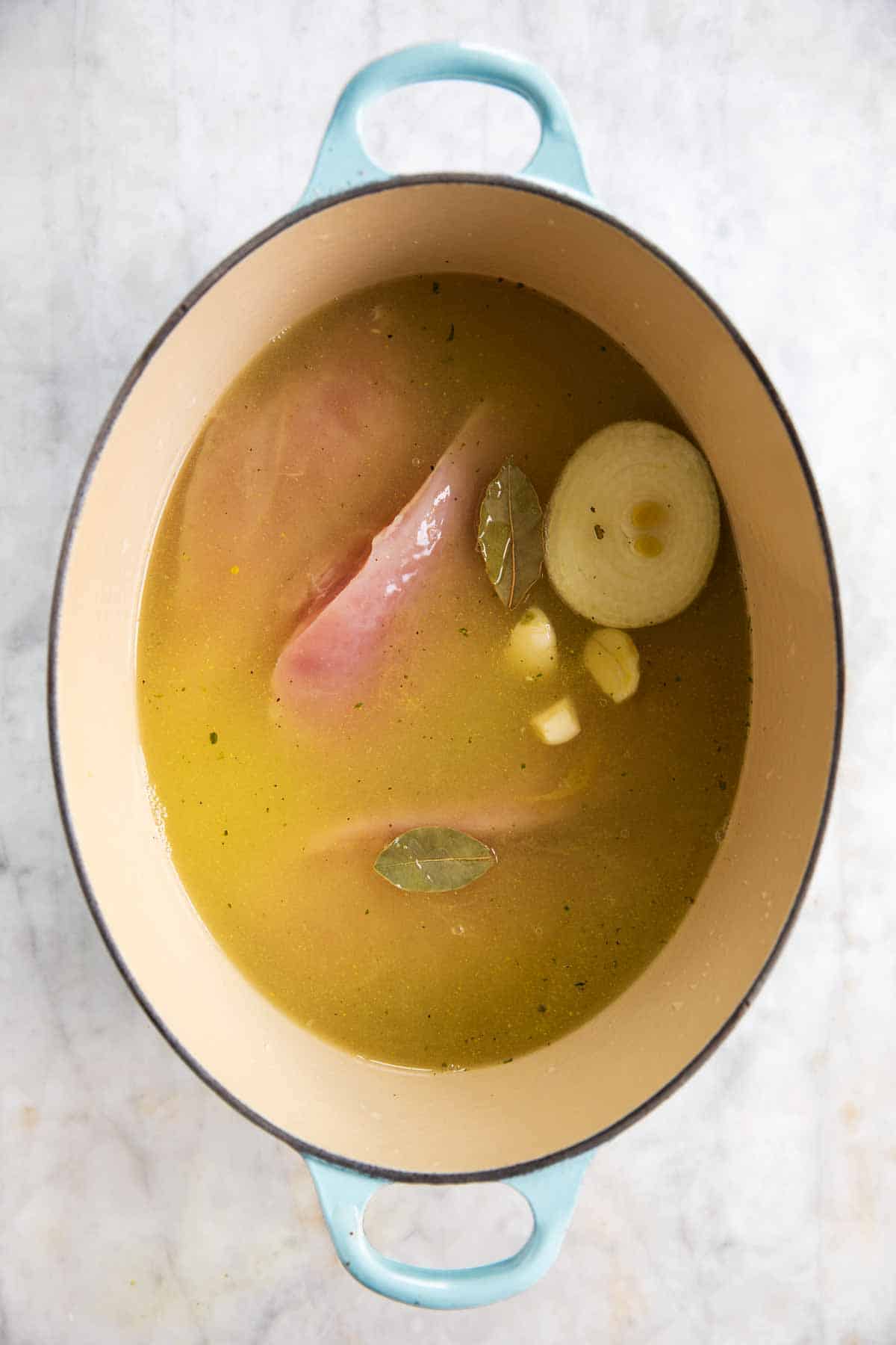 raw chicken in oval Dutch oven with broth and aromatics