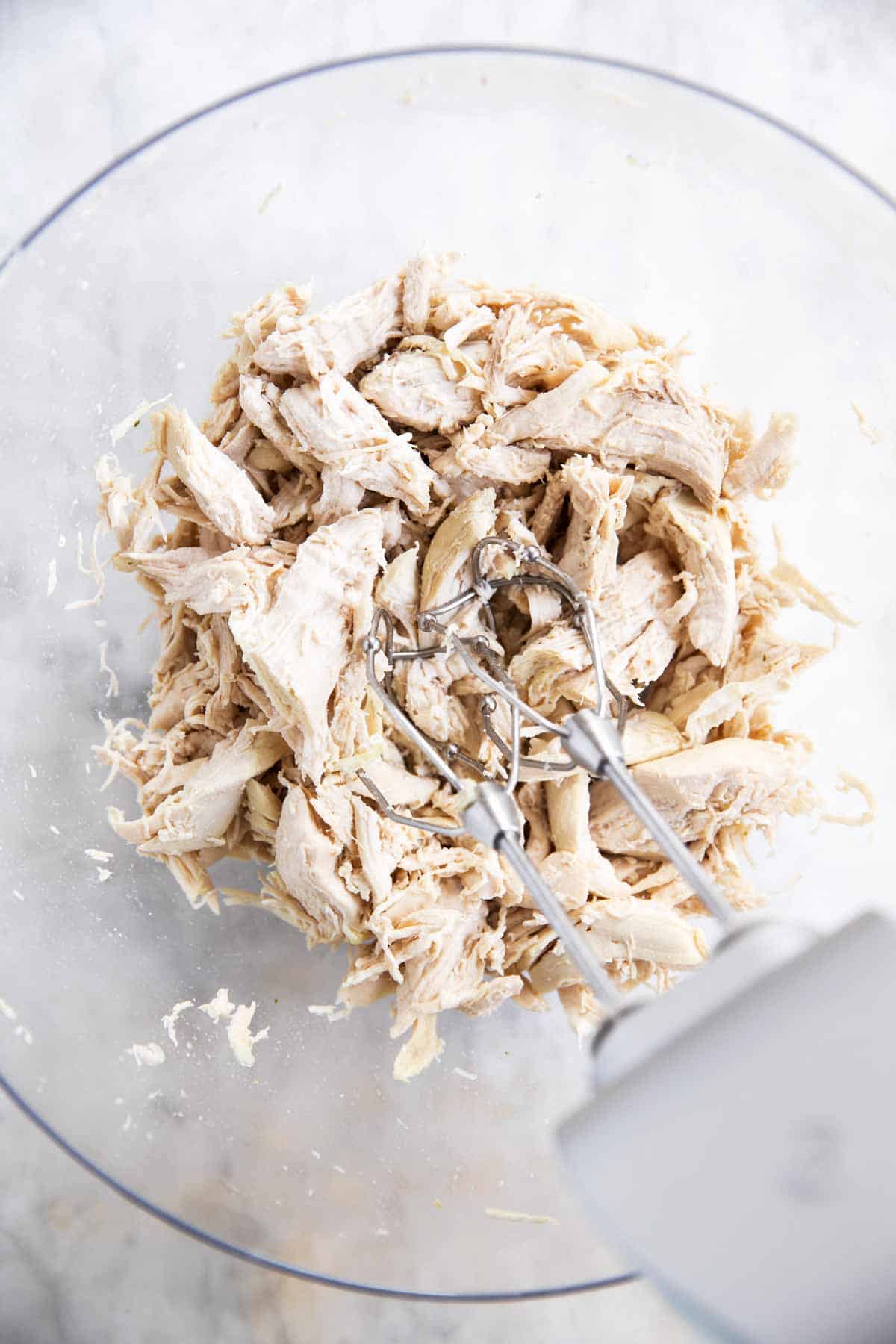 hand mixer beaters in glass bowl with shredded chicken