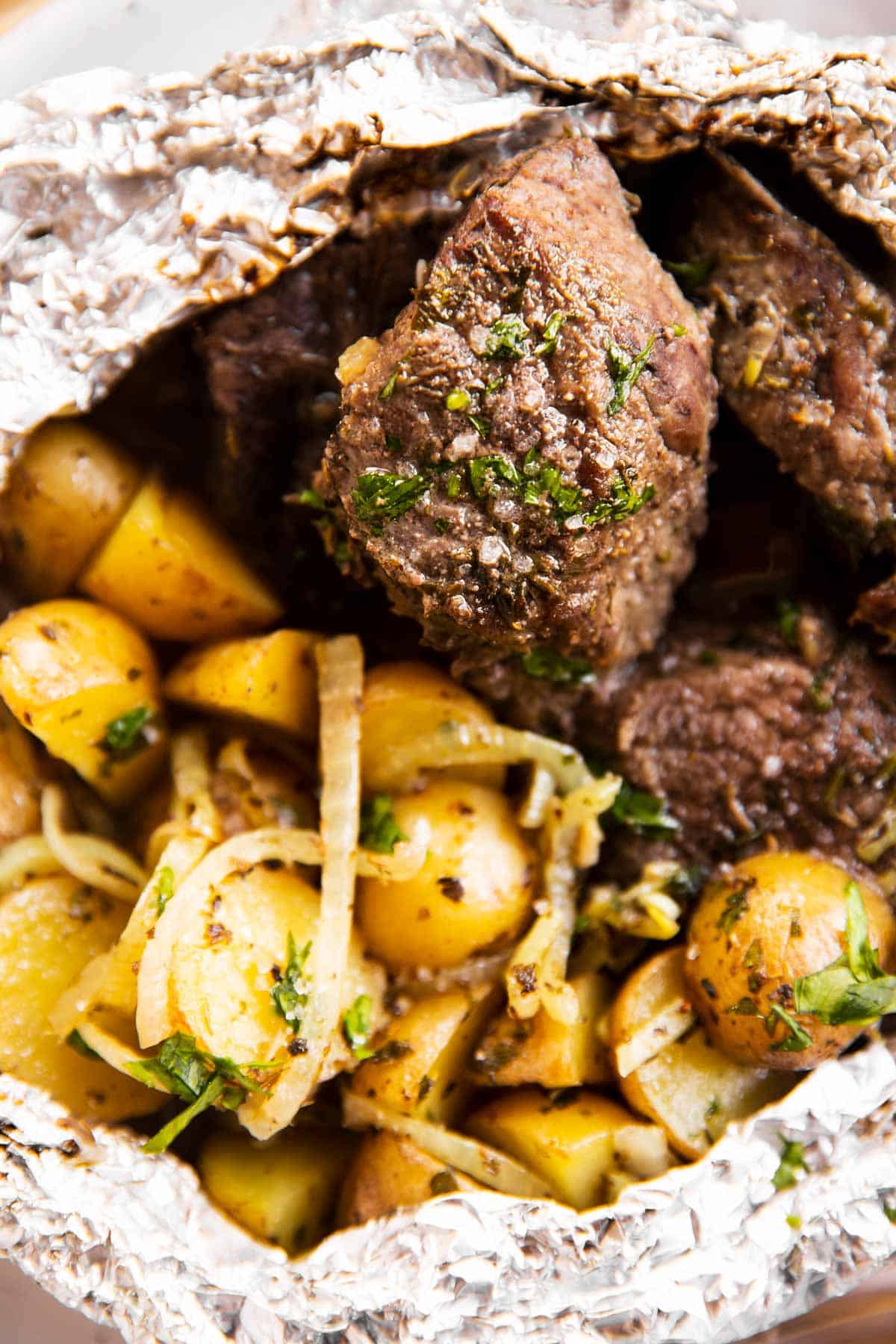 close up photo of steak and potatoes in foil packets