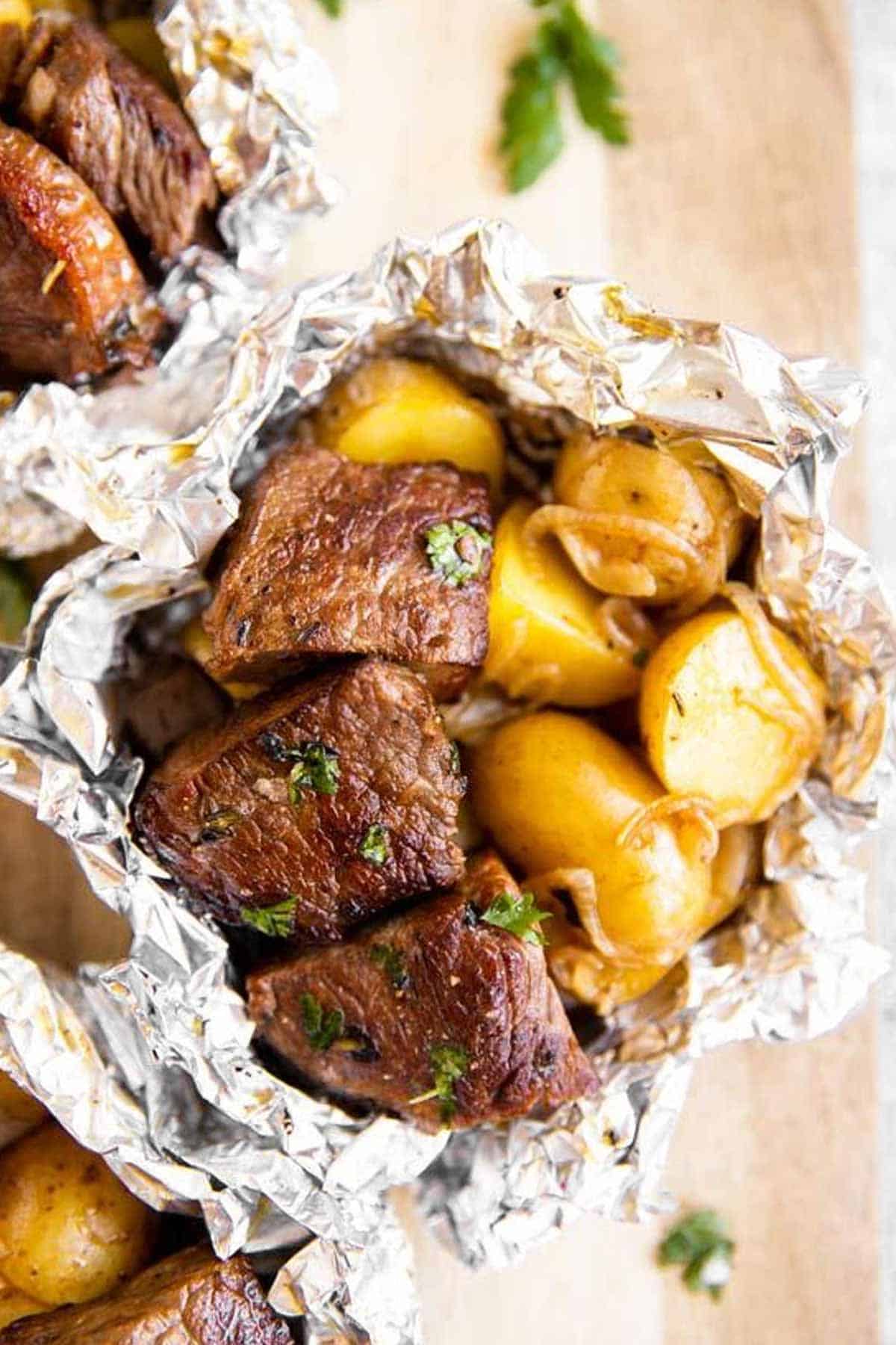 overhead view of a steak and potato foil packet on a wooden chopping board