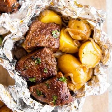 overhead view of a steak and potato foil packet on a wooden chopping board