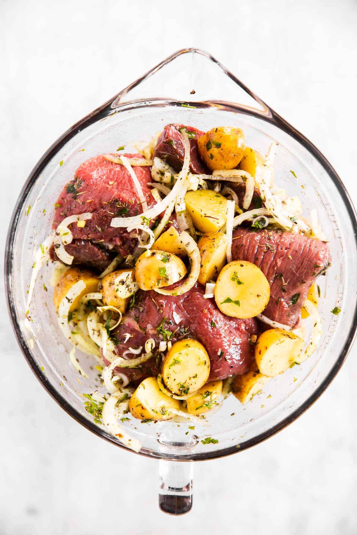 overhead view of steak, onion and potatoes with seasoning in glass bowl