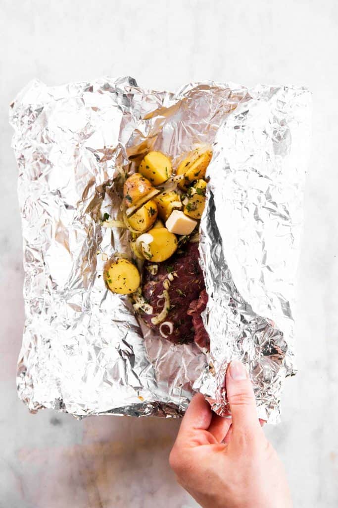 female hand folding foil over steak and potatoes