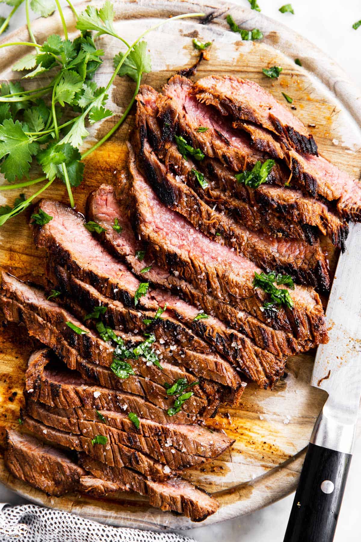 sliced flank steak on wooden board with fresh cilantro