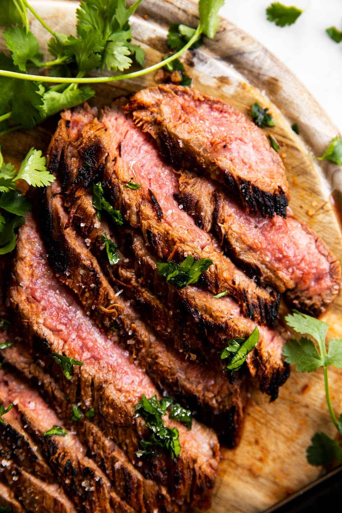 close up photo of sliced flank steak on wooden board with fresh herbs