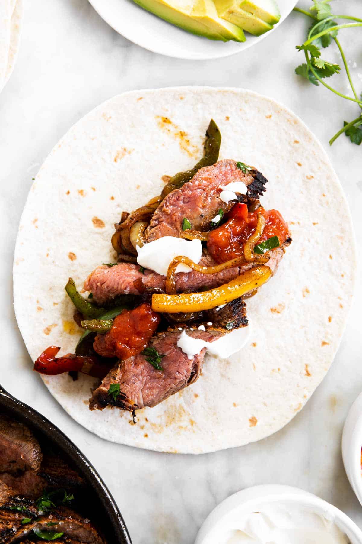 steak fajita filling in middle of flour tortilla surrounded by fajita toppings