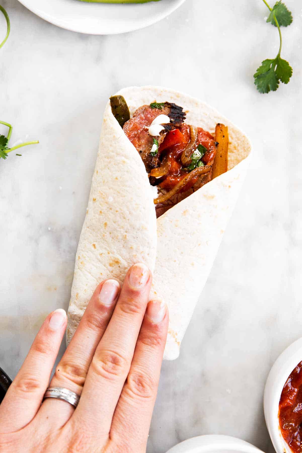 female hand folding steak fajita on marble surface