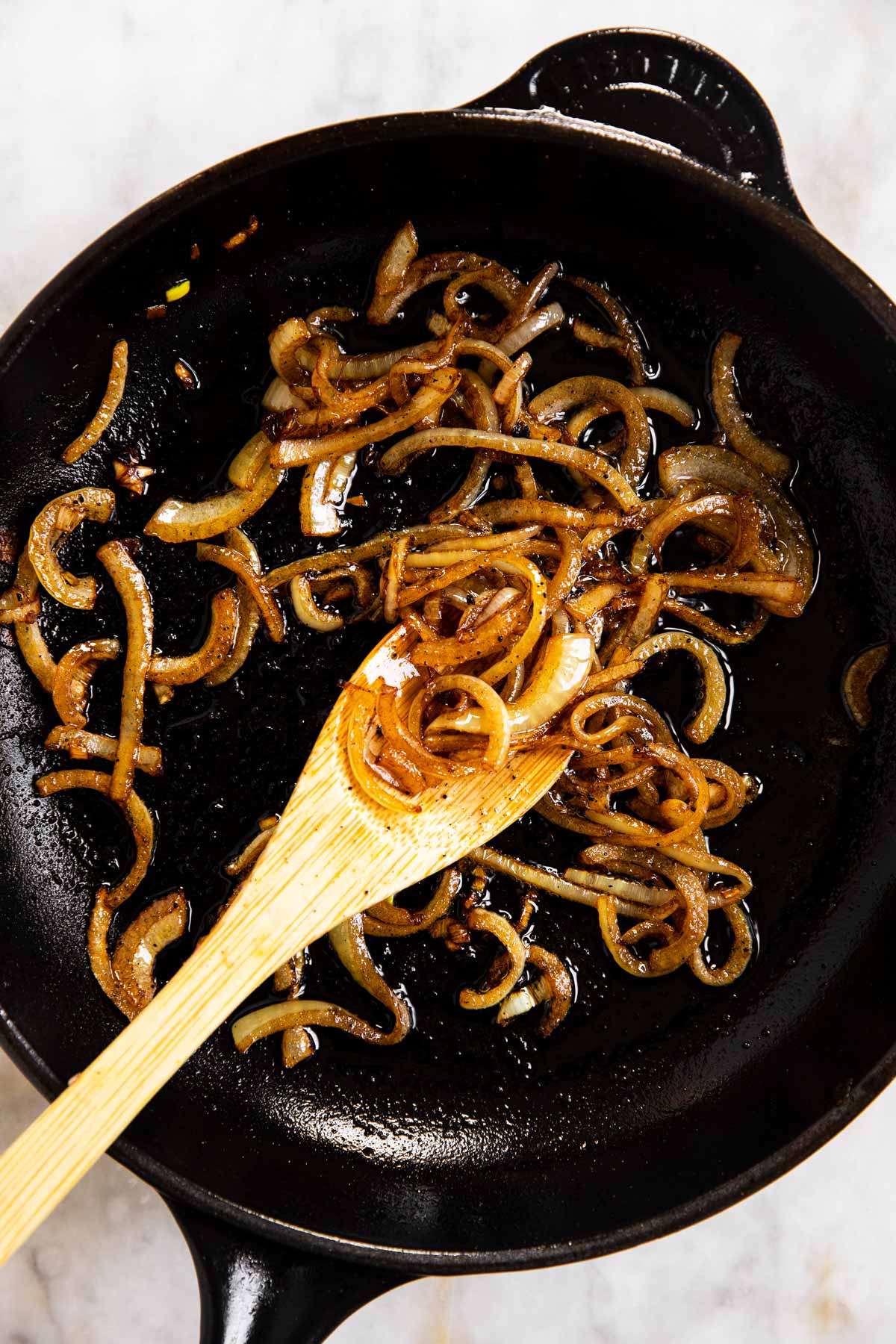 cooked onion in black cast iron skillet with wooden spoon