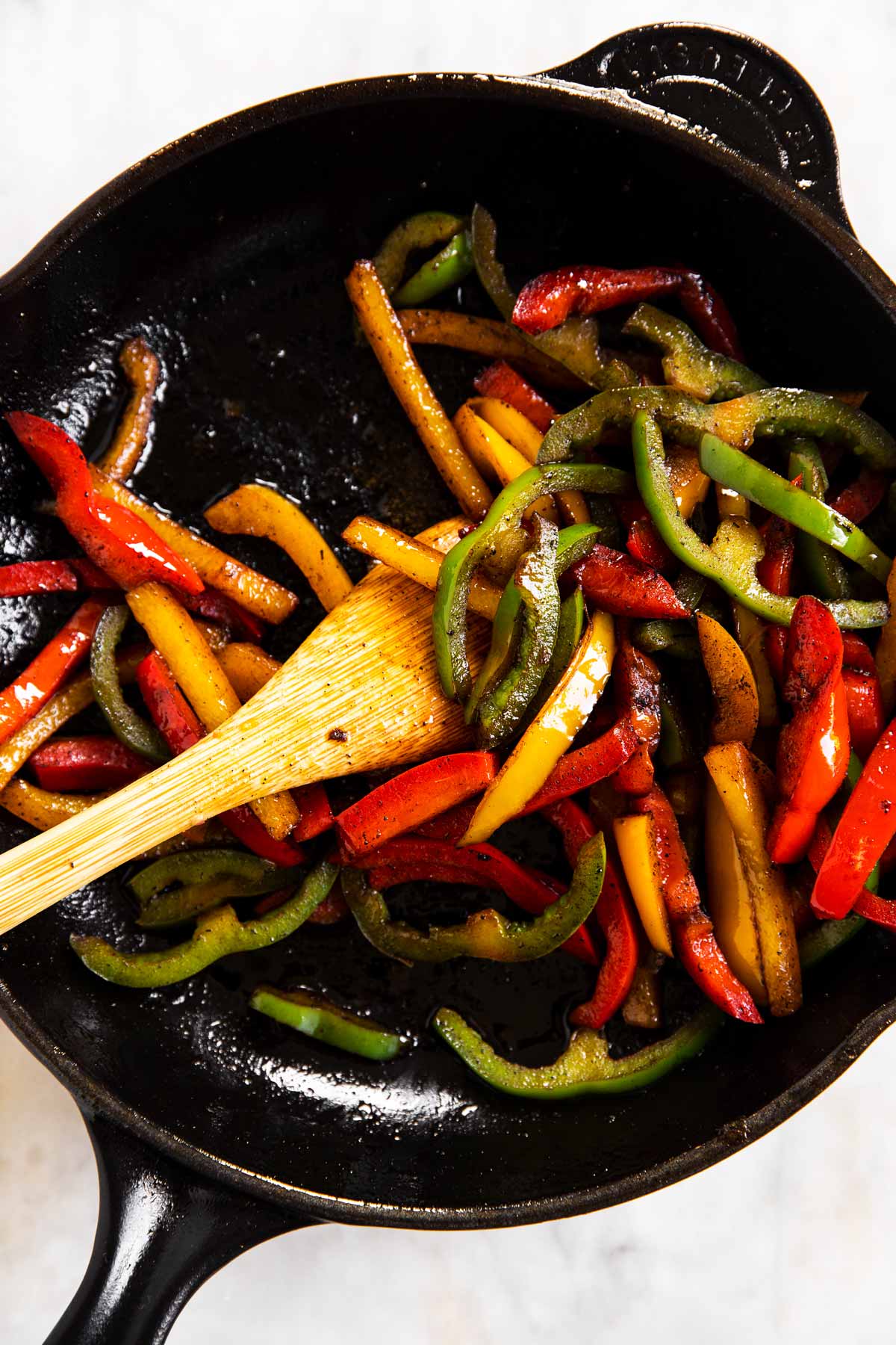 cooked bell peppers in black cast iron skillet with wooden spoon