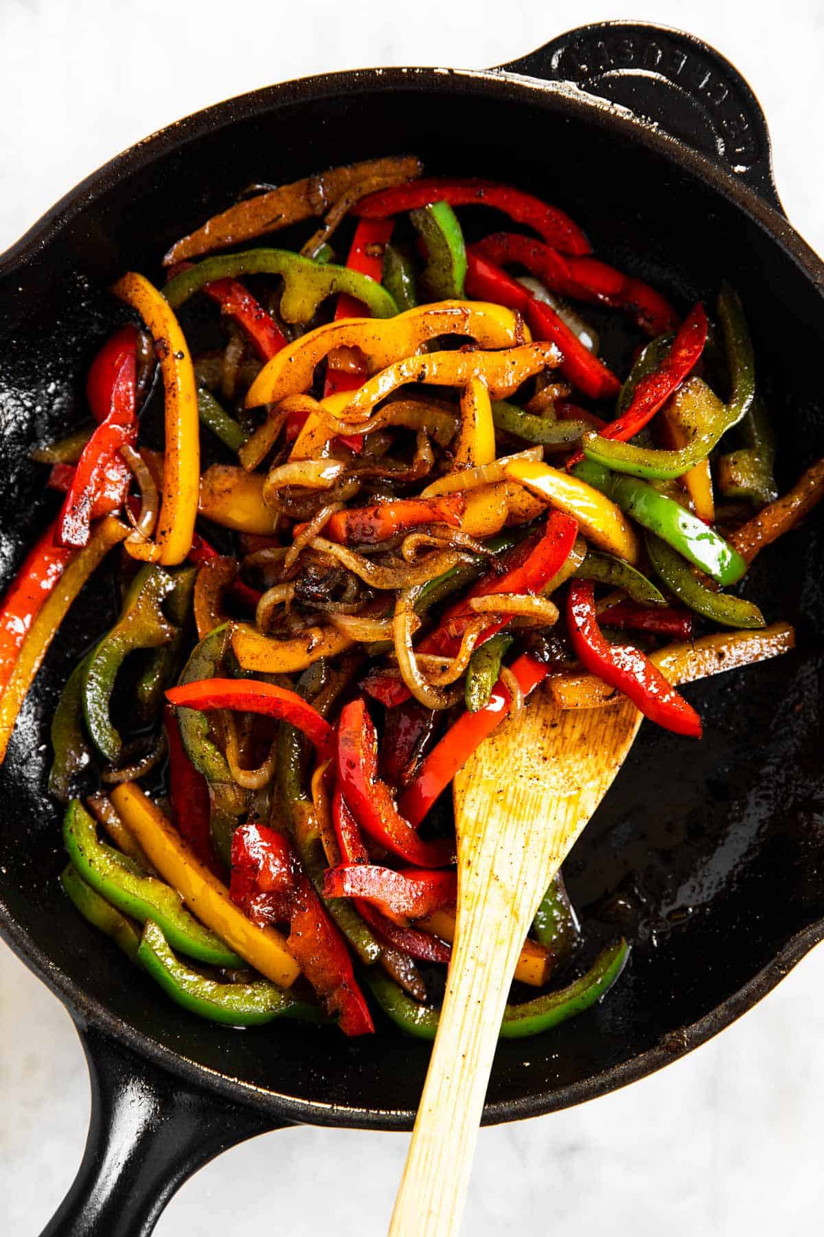 cooked onions and peppers in cast iron skillet with wooden spoon