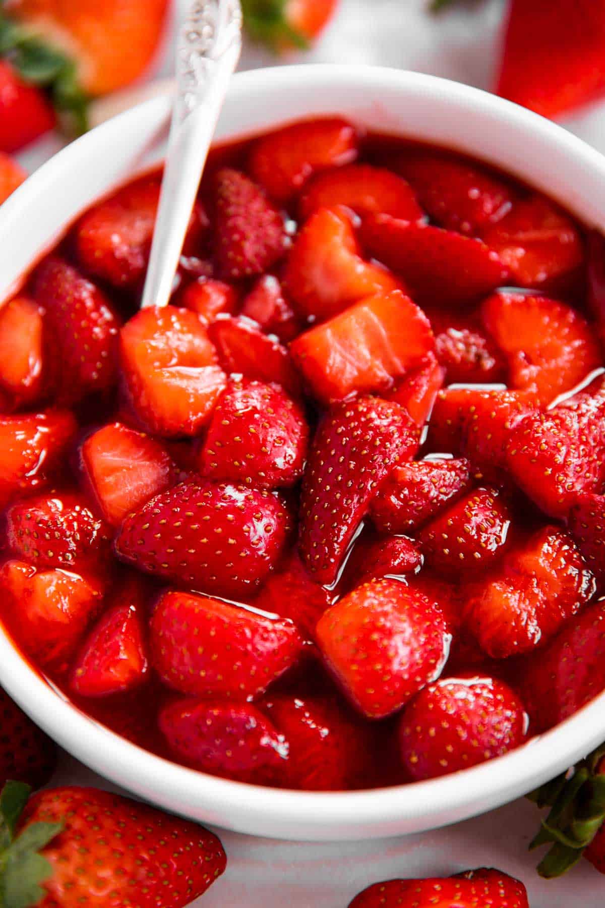 frontal view of strawberry sauce in white bowl, surrounded by more fresh strawberries