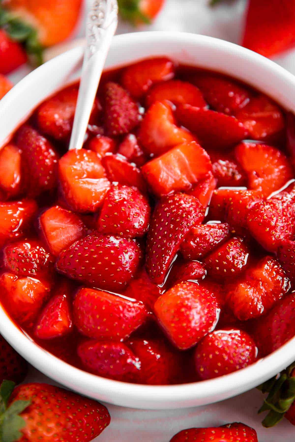 frontal view of strawberry sauce in white bowl, surrounded by more fresh strawberries