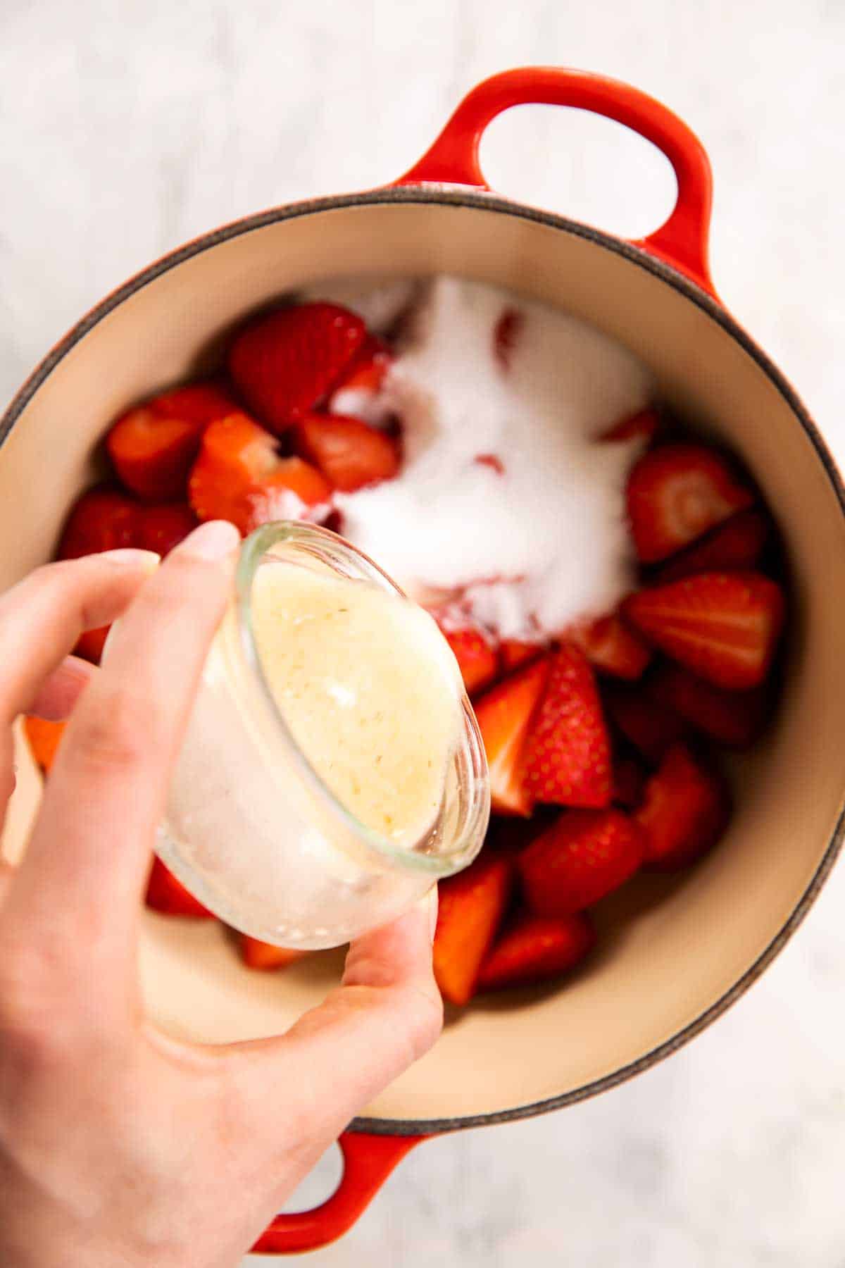 female hand pouring cornstarch slurry over strawberries and sugar in Dutch oven