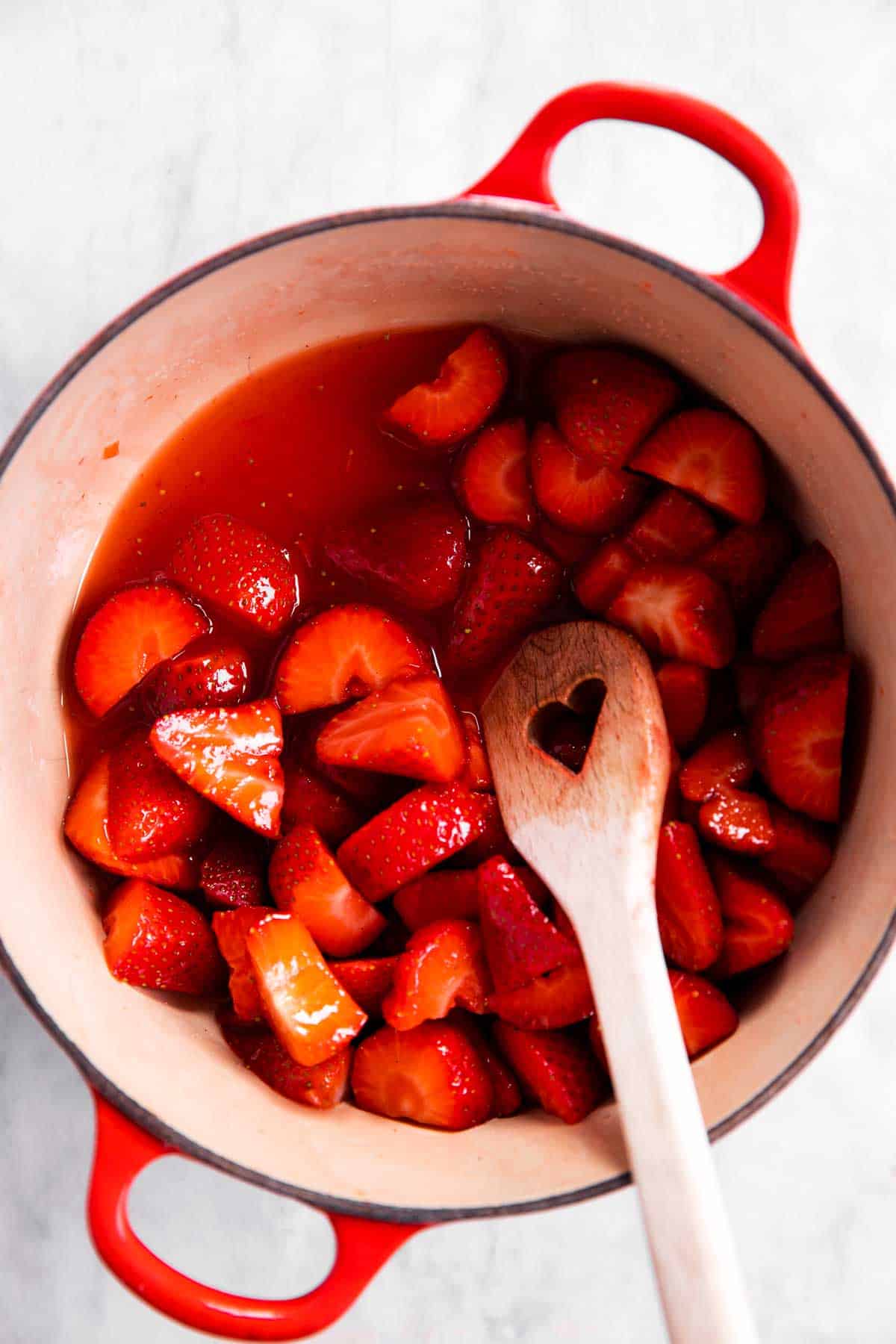 half-cooked strawberry sauce in Dutch oven with wooden spoon