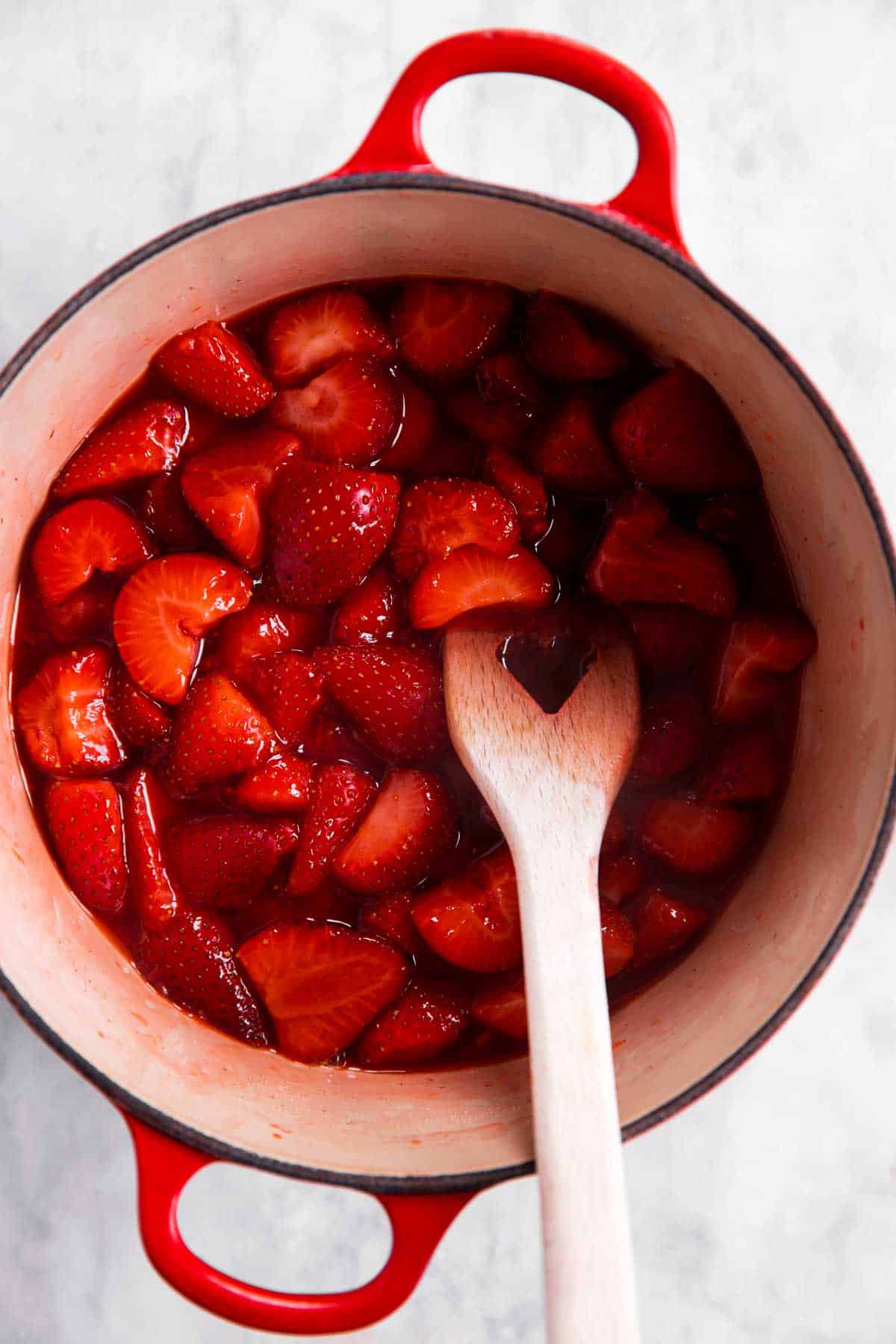 cooked strawberry sauce in Dutch oven with wooden spoon