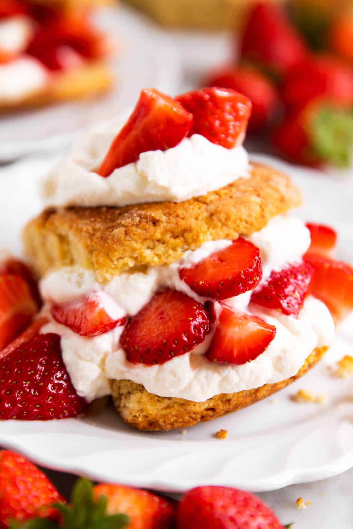 angled view of strawberry shortcake on white plate surrounded by fresh strawberries