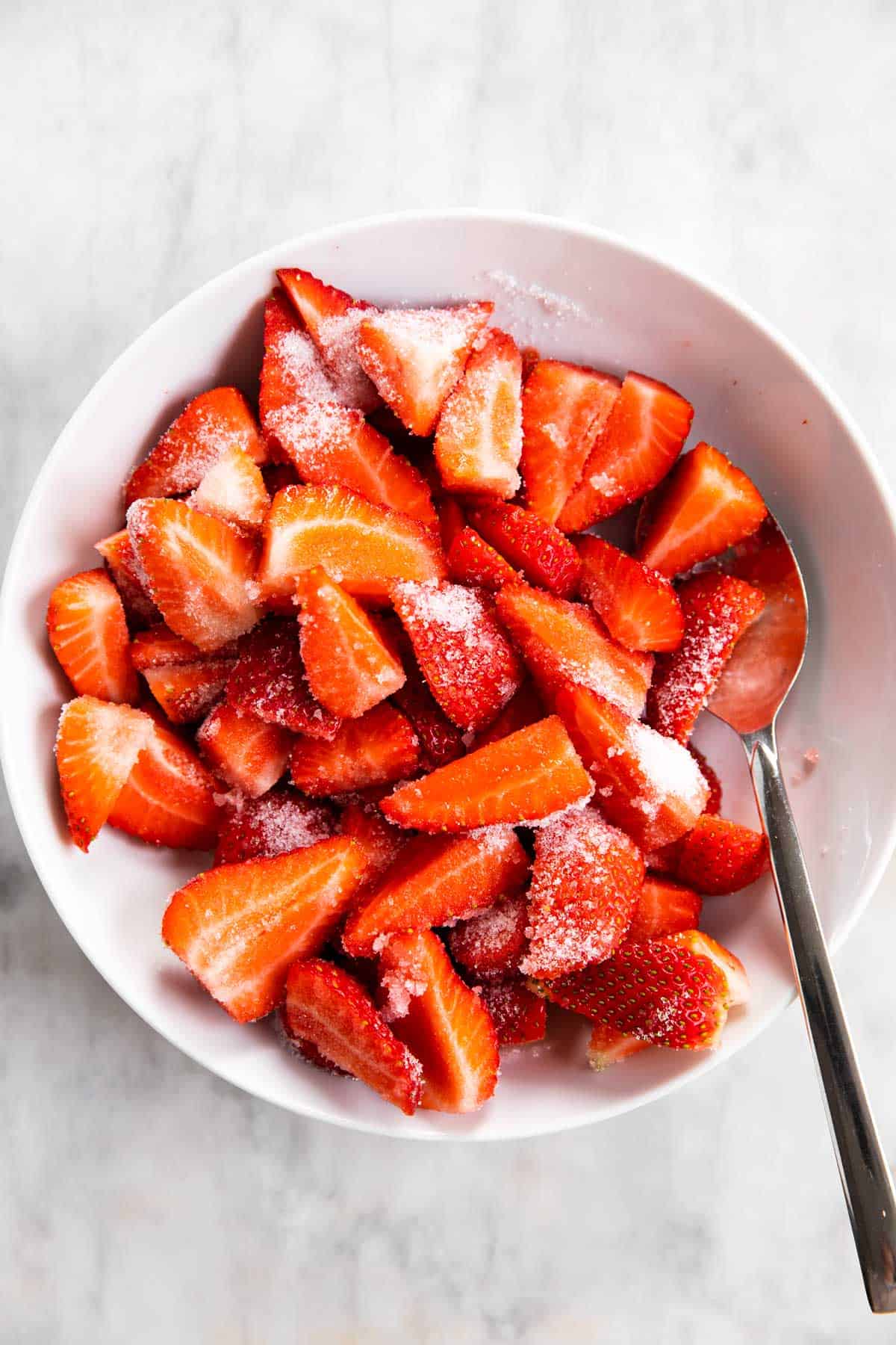 sliced strawberries in white bowl with sugar