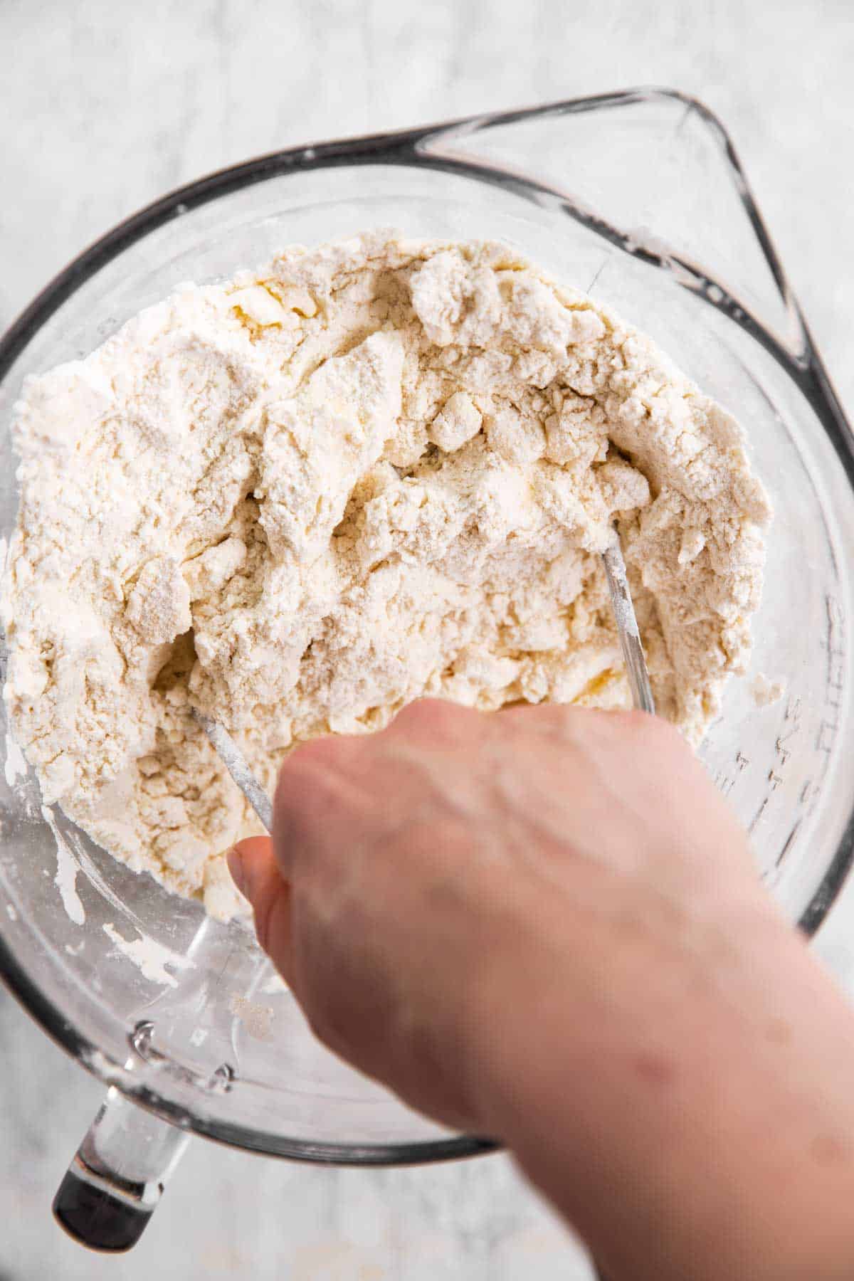 female hand using pastry cutter to blend butter into flour