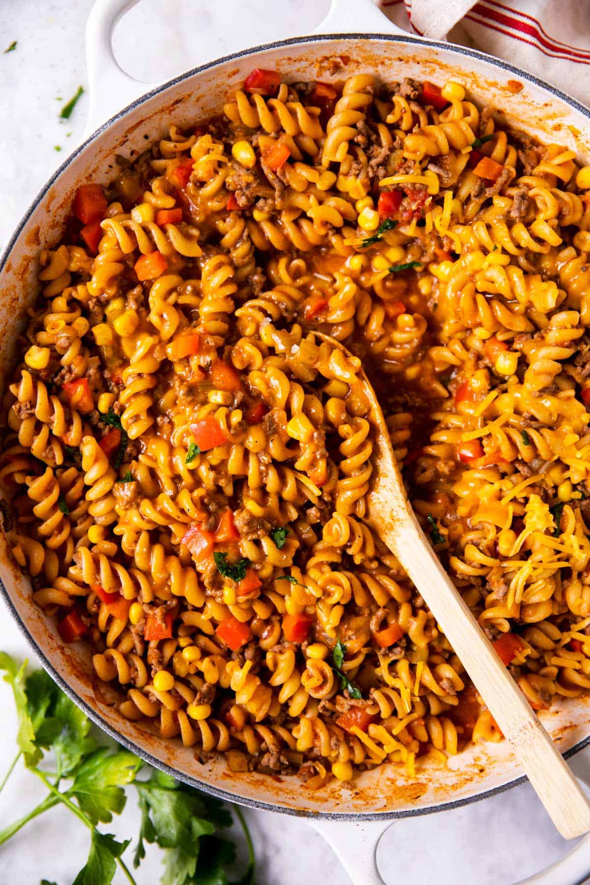 overhead view of taco pasta in white cast iron skillet with wooden spoon stuck inside