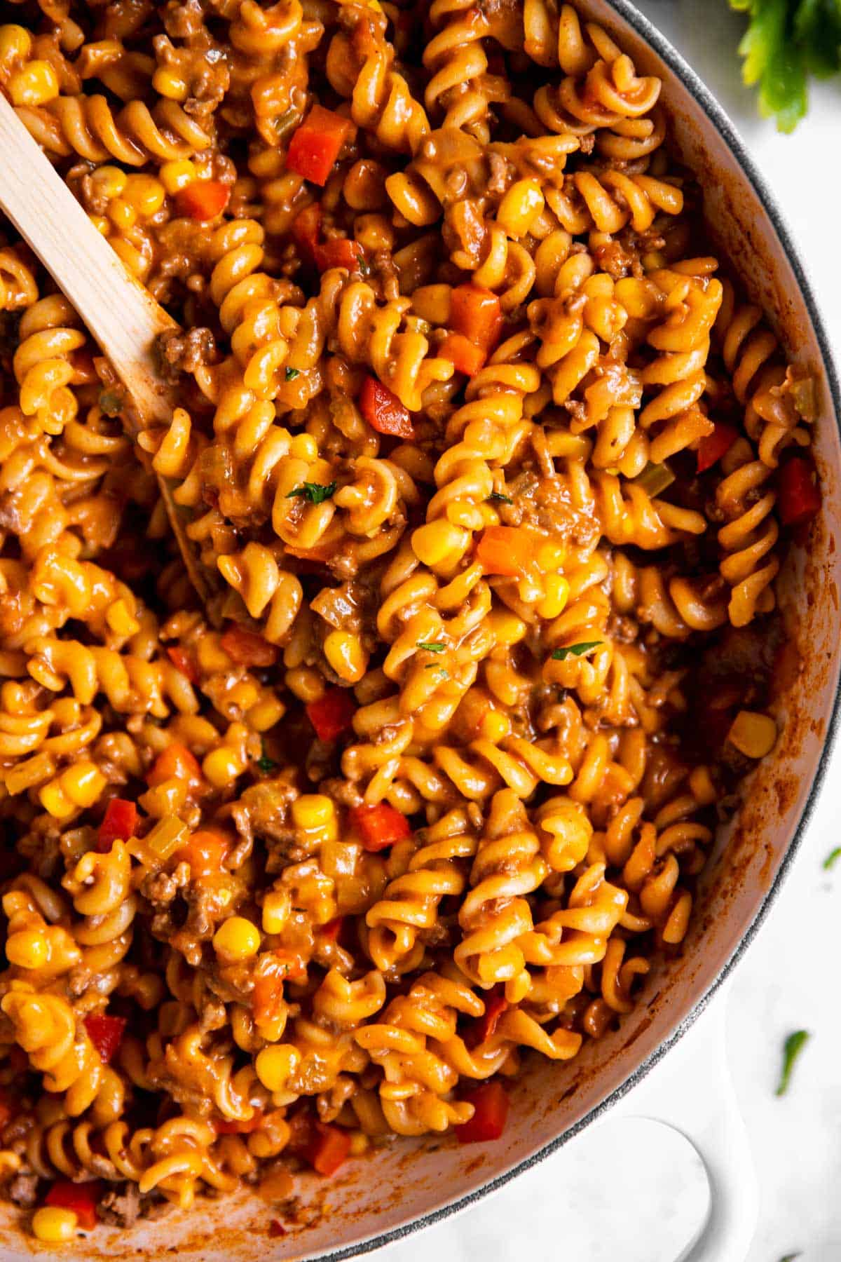 overhead close up of taco pasta in white skillet with wooden spoon