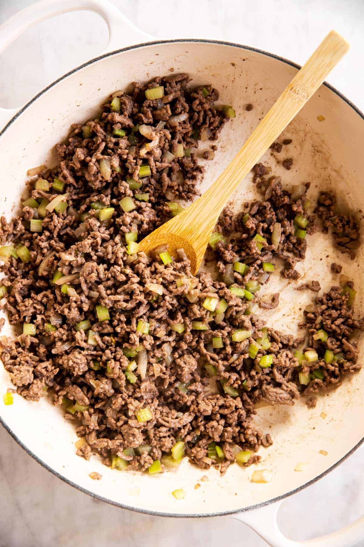 sautéed onion and celery with browned ground beef in white cast iron skillet