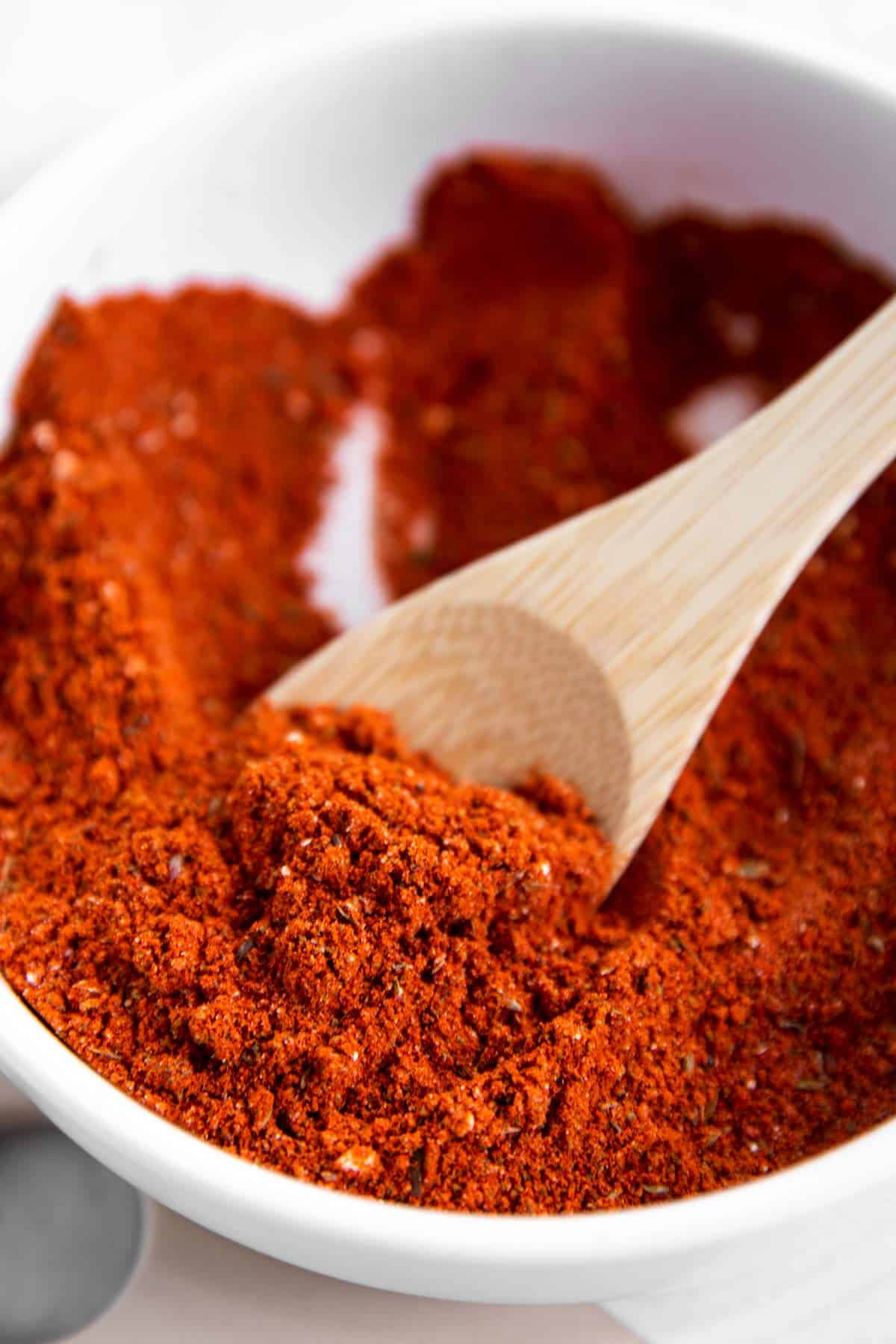 close up of homemade taco seasoning on small wooden spoon in white bowl